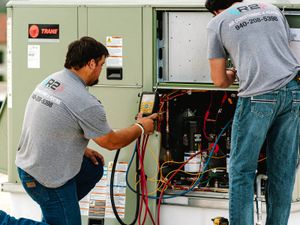 Two R2 technicians working inside an open rooftop air conditioning unit with gauges connected