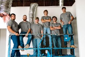 Six R2 Mechanical technicians standing on a scissor lift inside a commercial building under new ductwork