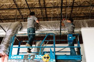 Two R2 technicians on a lift installing insulated ductwork in a commercial building