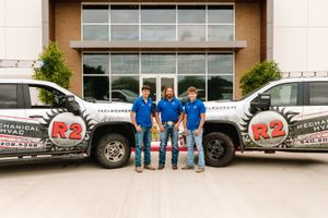 Three R2 Mechanical technicians standing between two wrapped service trucks